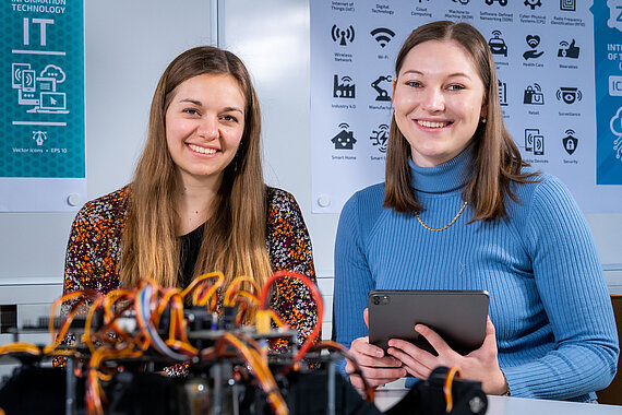 Zwei Studentinnen aus dem Bereich Infromatik mit Tablet in der Hand und einem programmierten Roboter