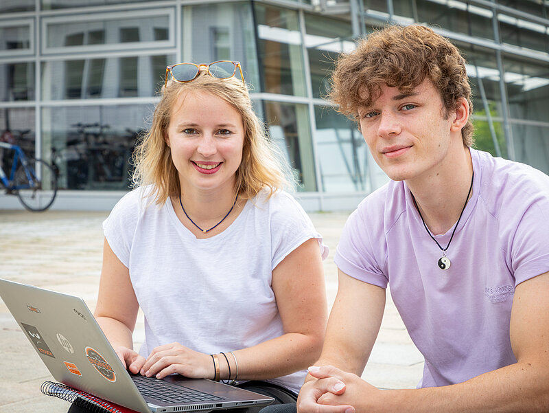 Studentin und Student mit Laptop vor einem Hochschulgebäude