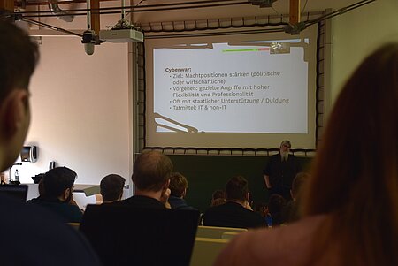 Blick in den Hörsaal (von hinten zur Präsentation). Referent Florian Oelmaier spricht zum Thema Cyberwar.