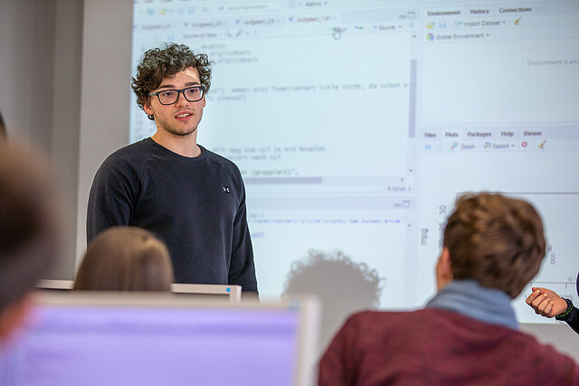 Student steht vor Leinwand und präsentiert seine Ergebnisse