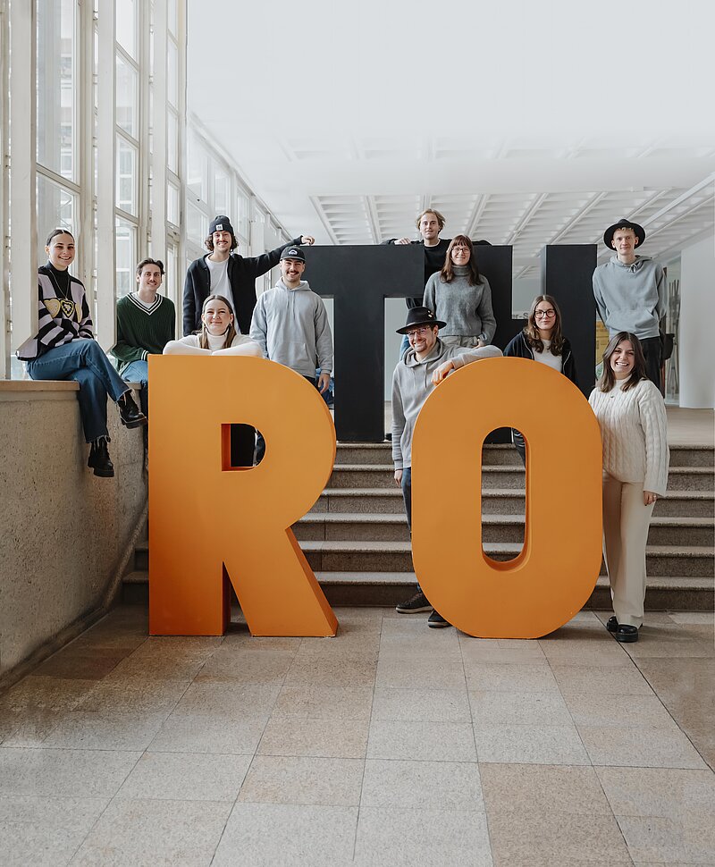 Students in standing and sitting between giant letters T, H, R, O