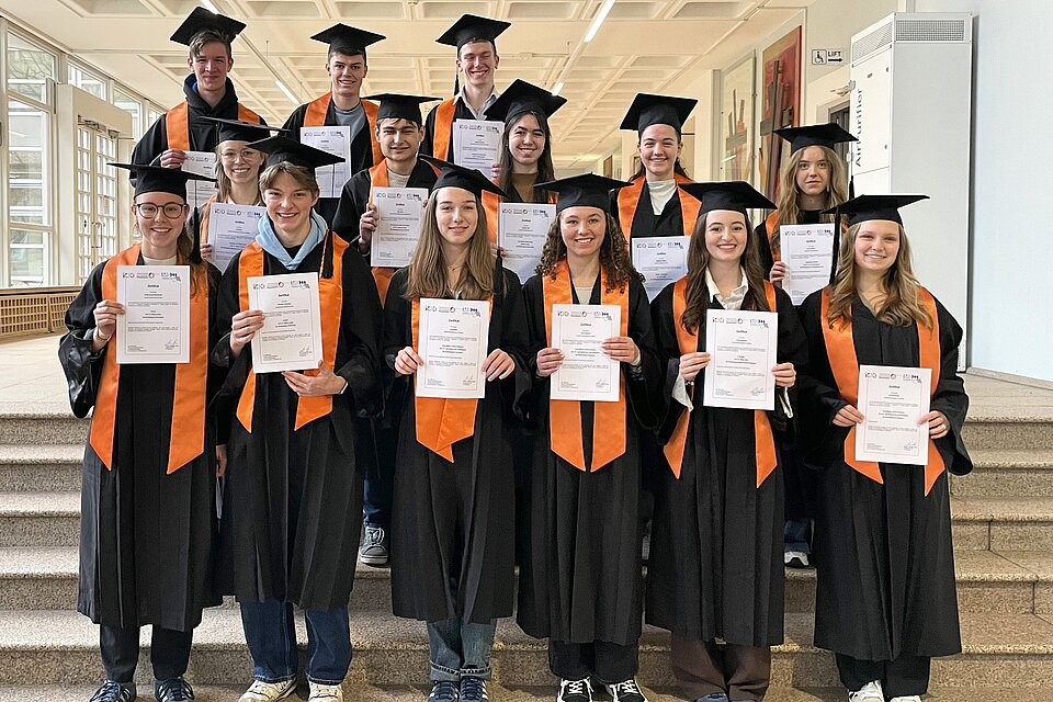 Auf de Foto sind die 17 Frühstudierende in schwarzen Talaren und mit ihren Urkunden zu sehen.