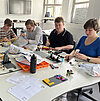 Das Bild zeigt Studierende, die an einem Tisch sitzen und mit Legosteinen bauen.