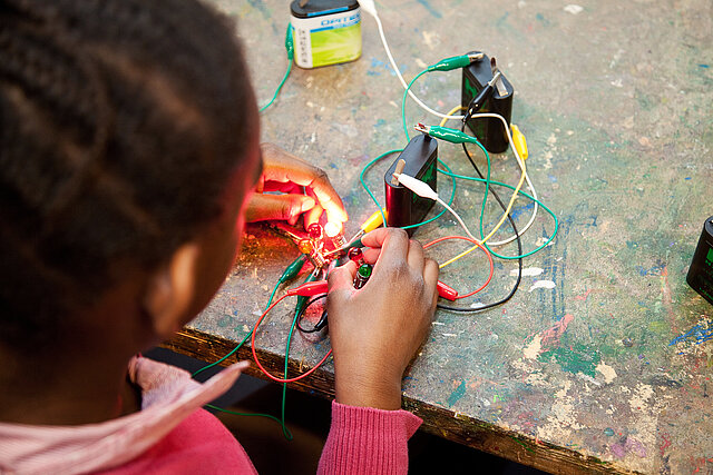 Kind experimentiert mit Batterien, Kabeln und Lämpchen