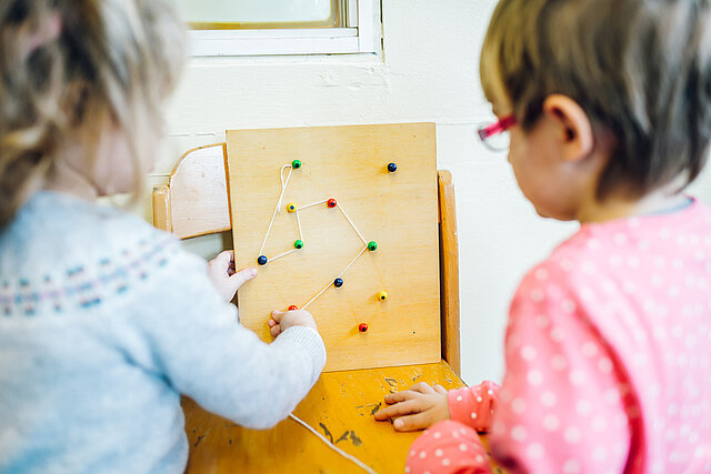 Zwei Kinder spannen Wollfäden auf einem Brett mit bunten Pins