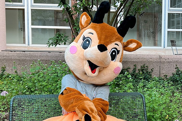 Gämse-Maskottchen sitzt auf einer Bank vor der Hochschule