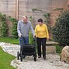 älterer Herr geht mit Rollator durch einen Garten spazieren