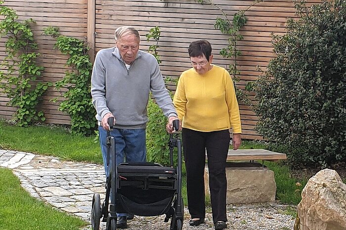 älterer Herr geht mit Rollator durch einen Garten spazieren